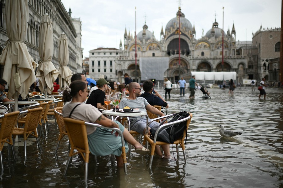People sit at outdoor café tables in a partially flooded Venice square.