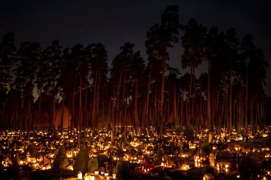 Hundreds of candles and lanterns illuminate graves in a cemetery.