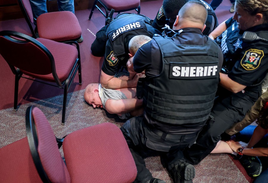 Several police officers hold a man on the ground while arresting him in a meeting room.