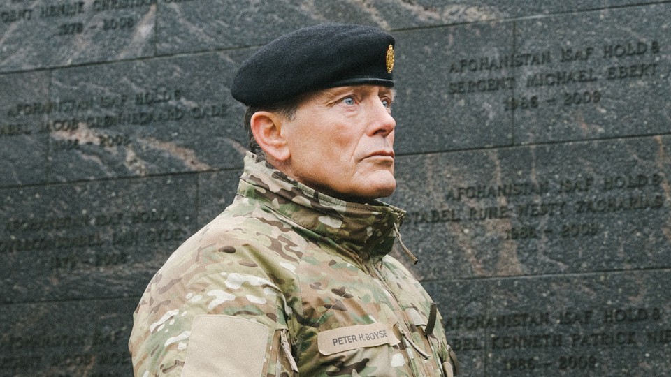 a color photograph of Denmark's military chief wearing fatigues and beret in front of a national war memorial