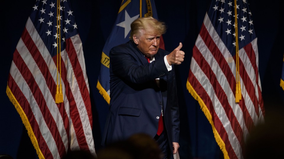 Standing in front of three flags, Donald Trump gives a thumbs-up.