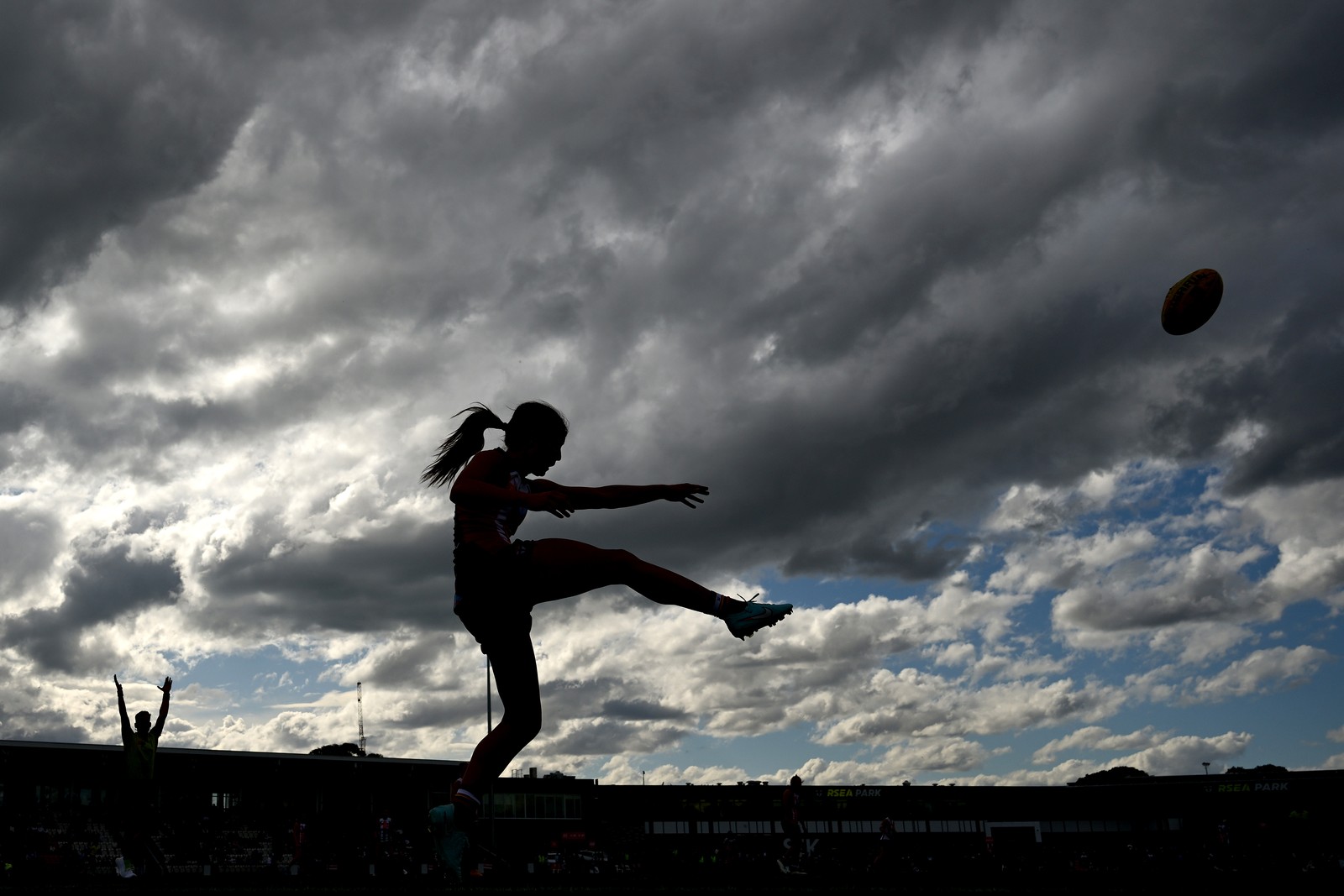 A football player kicks a ball, seen in silhouette.
