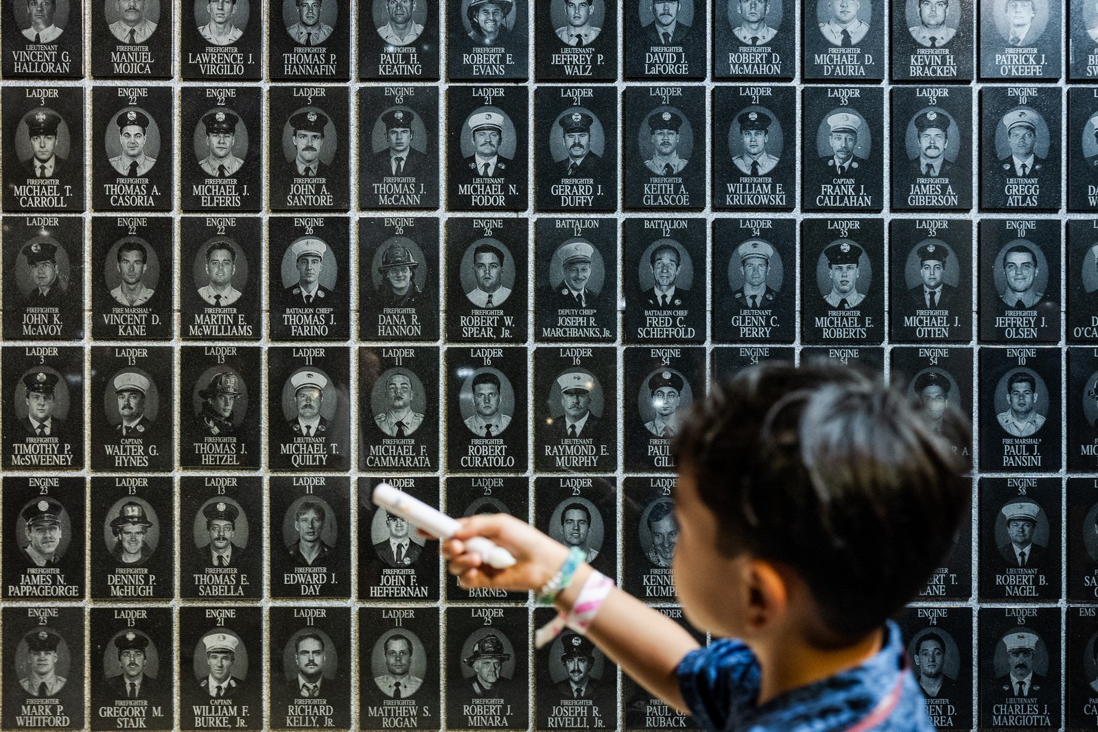A young boy uses a candle to count the faces of fallen firefighters placed on a memorial wall.