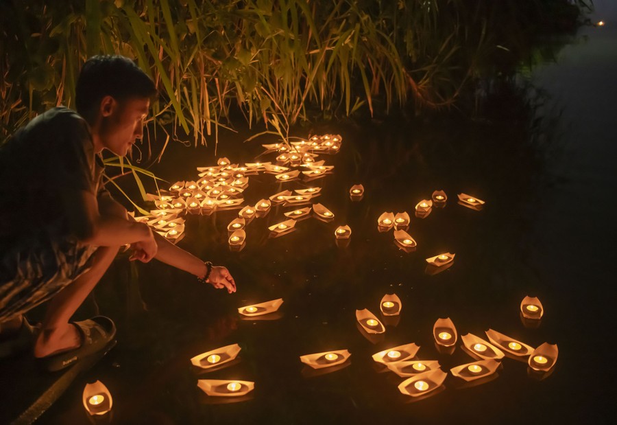 A person leans down over a cluster of small floating candles.