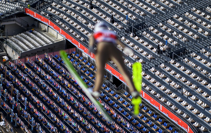 A ski jumper is seen in midair, with hundreds of empty seats below them.