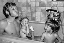 Black-and-white photograph of a dad and two sons in the bath, the dad spitting water out of his mouth