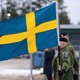 Soldiers stand next to a Swedish flag.