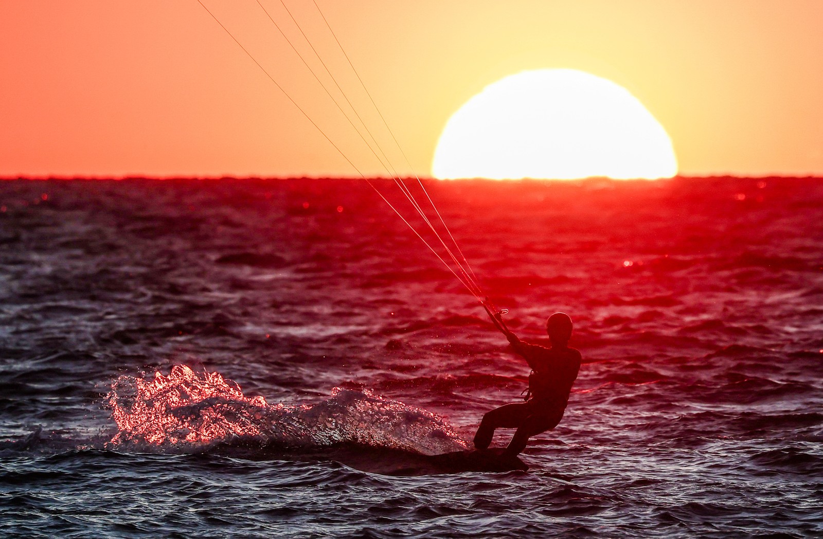 A kitesurfer surfs at sunset.