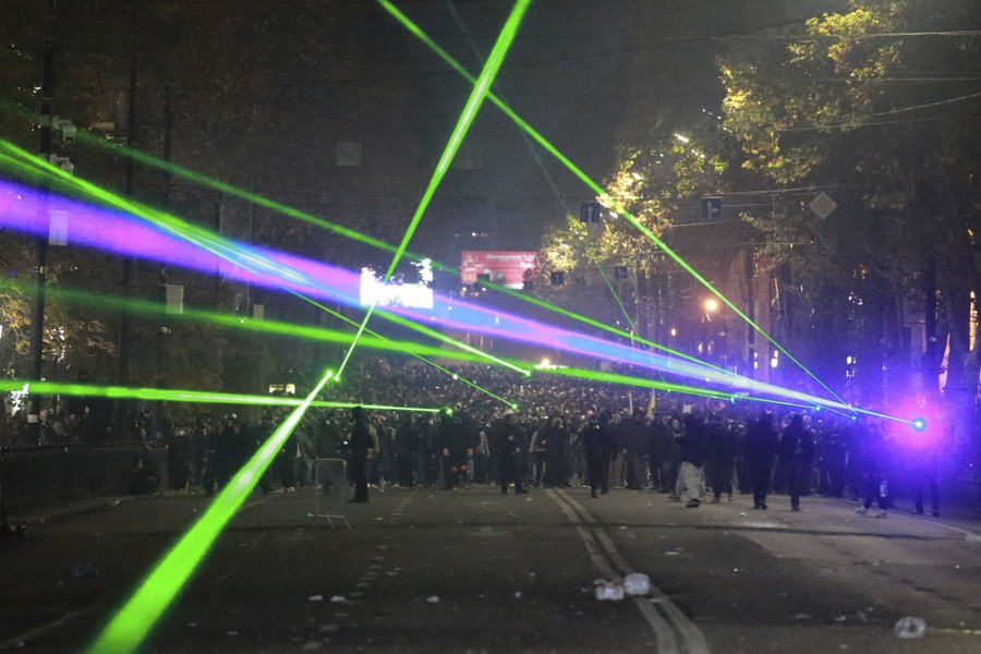Demonstrators point green lasers toward police in a city street.