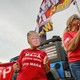Photograph of three women at a Trump rally flying signs and banners. The woman in the center is wearing a Trump mask and a MAGA T-shirt.