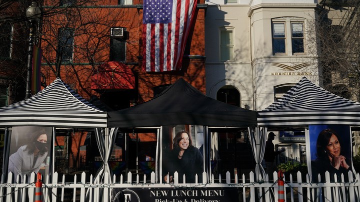 Large photos of Vice President Kamala Harris hang outside a restaurant in Washington, D.C. Hanging off a building in the background is a giant American flag.