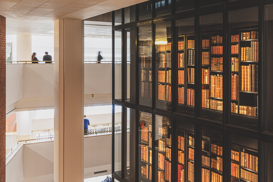 photo of interior of library showing two floors of an atrium-like space, with people at railings overlooking the historical collection in a glassed-in central column