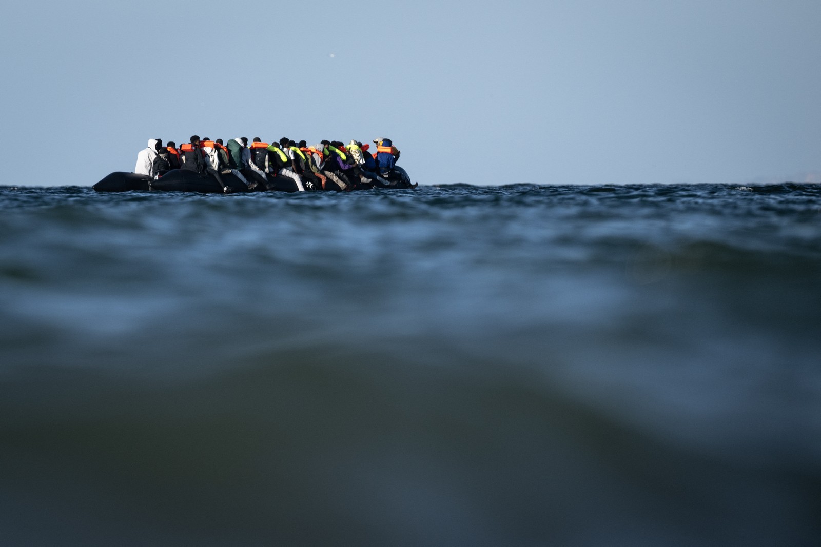 A low-angle view of many migrants wearing life vests sitting on an inflatable raft in the ocean