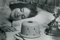 A black-and-white image of a woman sleeping next to a sound conditioner