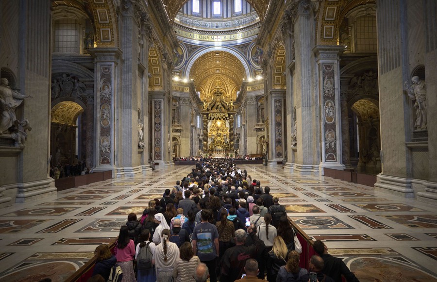 A crowd waits in a long line inside of a large, ornate basilica.