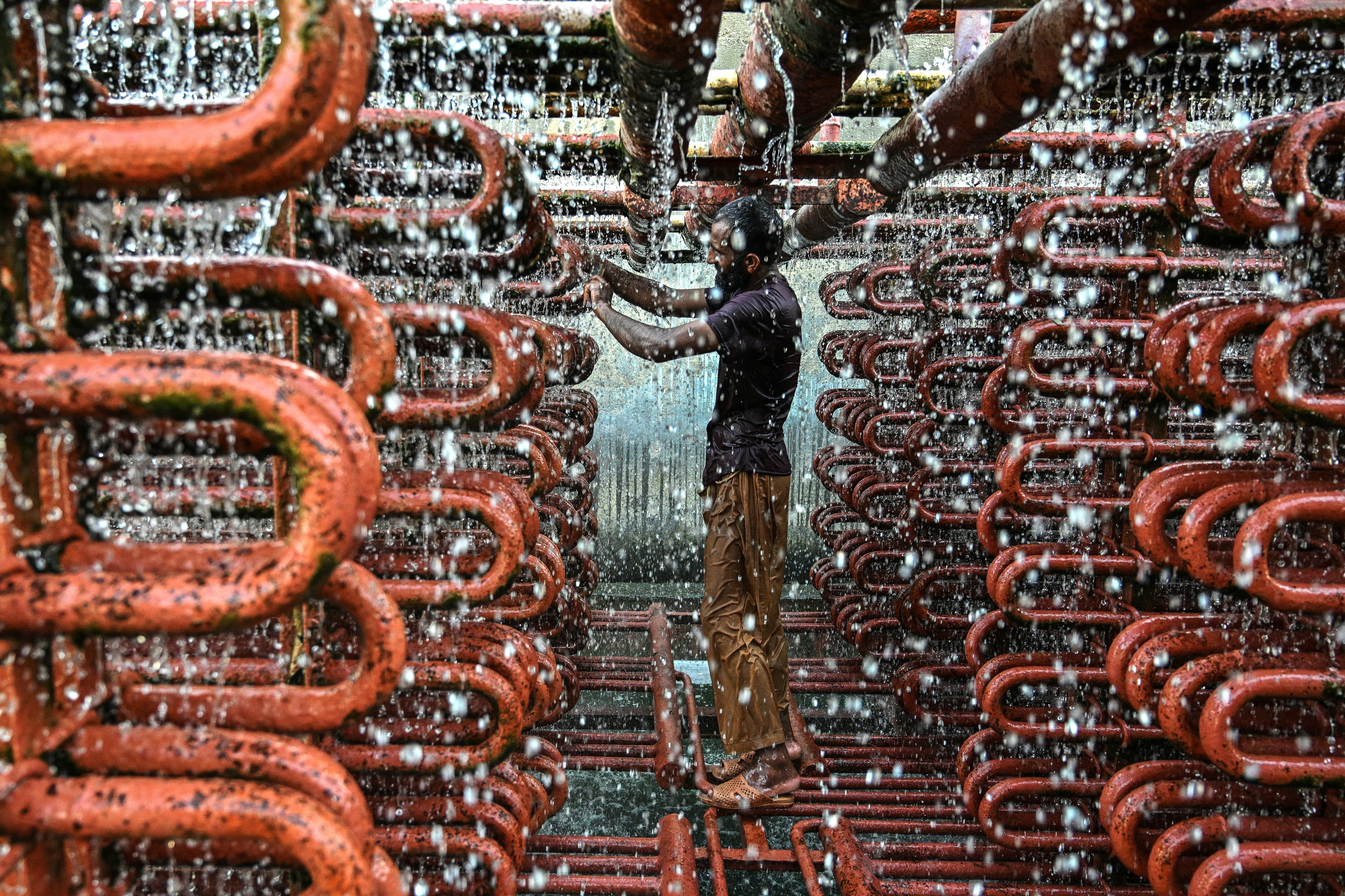 A man stands in many pipes, soaked in dripping water.