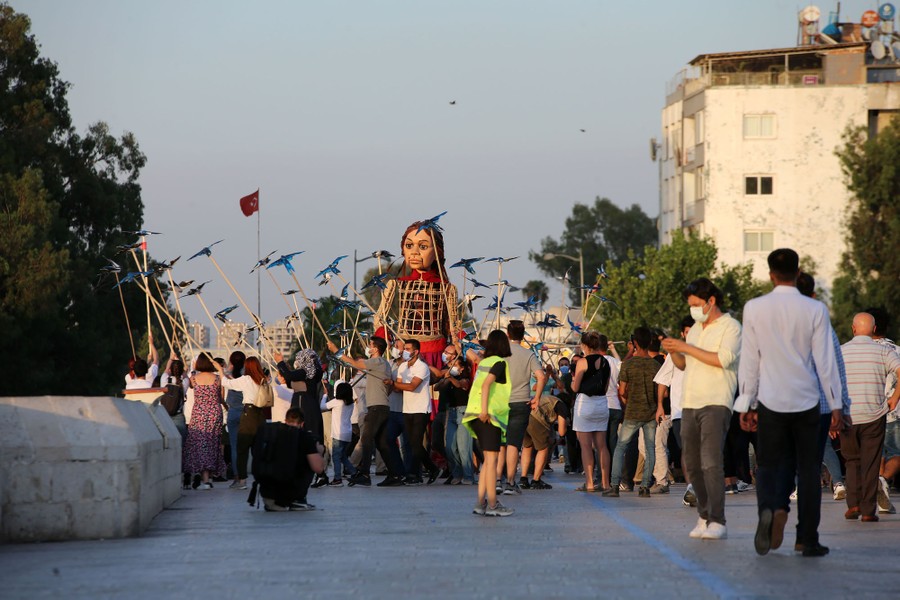A tall puppet of a girl walks alongside people carrying bird puppets on sticks.