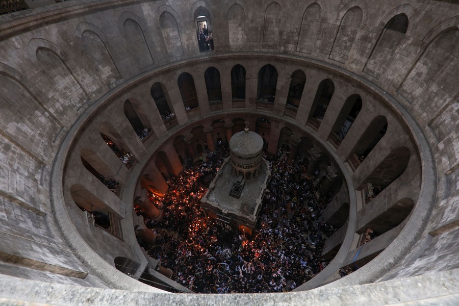 A view into the interior of a dome, with a small shrine inside surrounded by people with lit candles.
