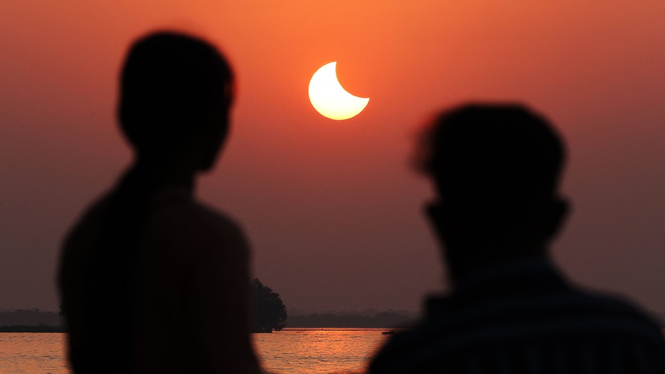 The silhouette of two people watching a partial solar eclipse in a deep-orange sky