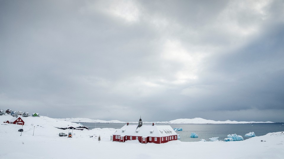 A dark-red house surrounded by snow stands in front of a body of water