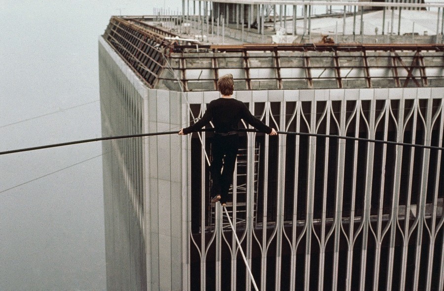 A tightrope walker inches along a cable strung between two skyscrapers.