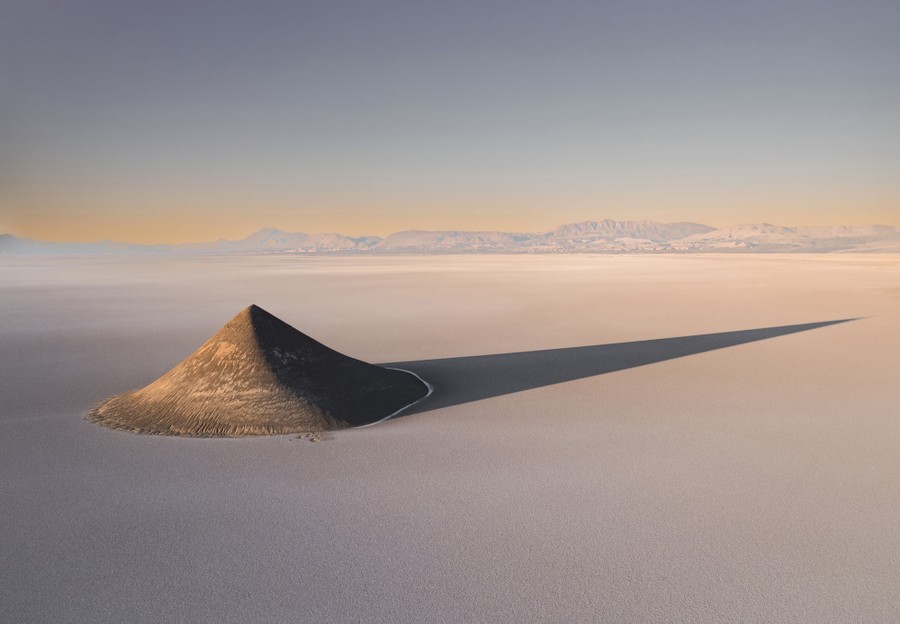 An aerial view of a cone-shaped mountain standing on a broad salt plain