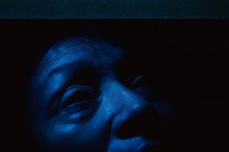 the top half of the photo shows an upside down landscape, with clouds above mountains and a dark starry sky above that. the sky bleeds into an image of a person's face in the dark