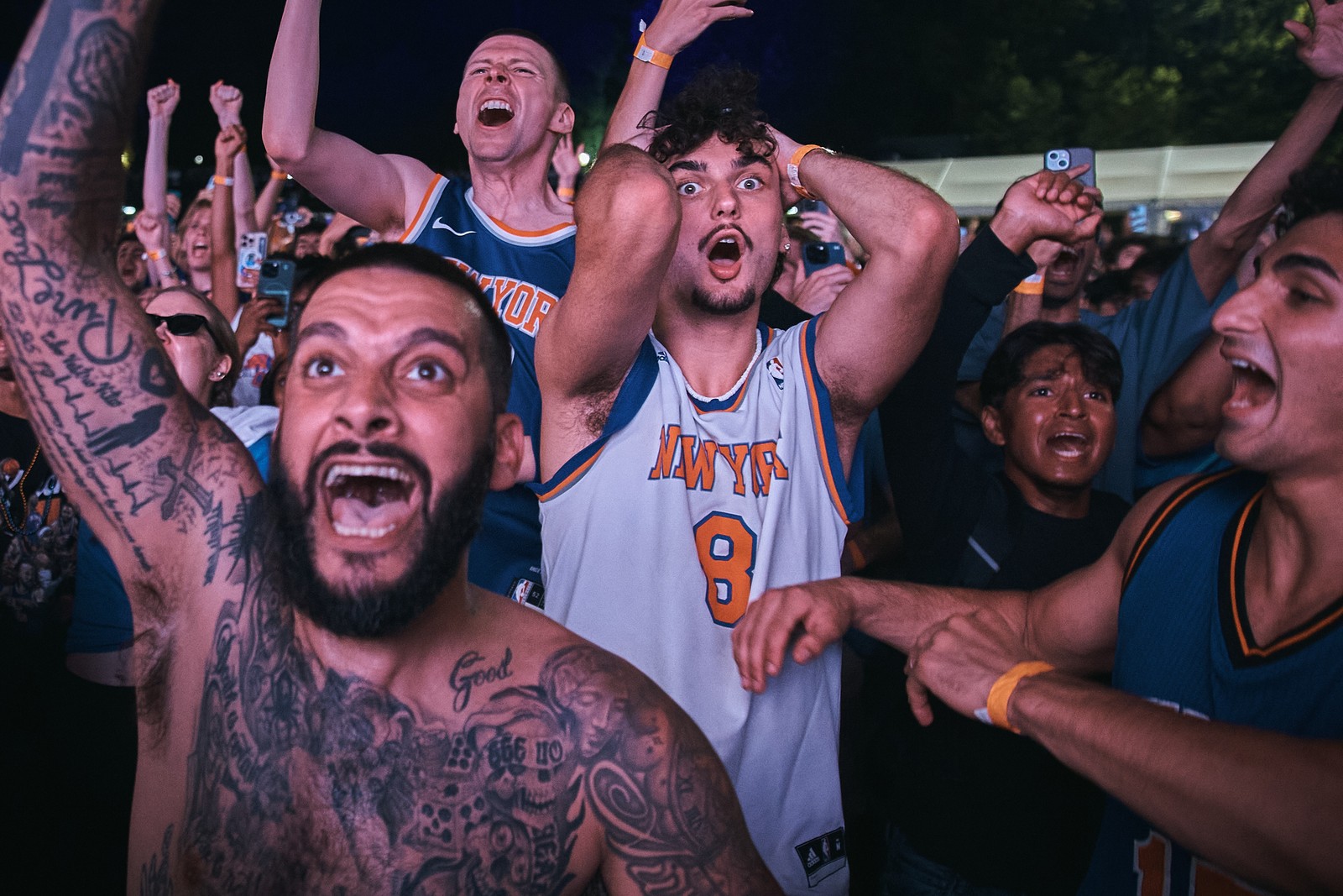 A group of basketball fans at a watch party cheer and raise their arms.