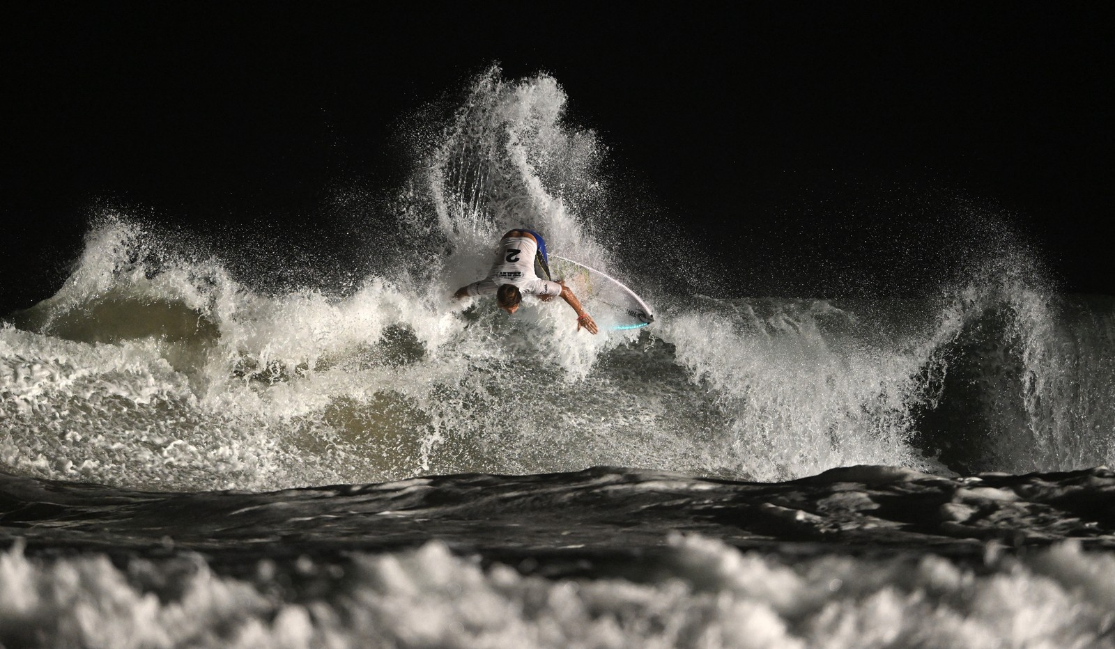 A person rides a surfboard on a wave at night.