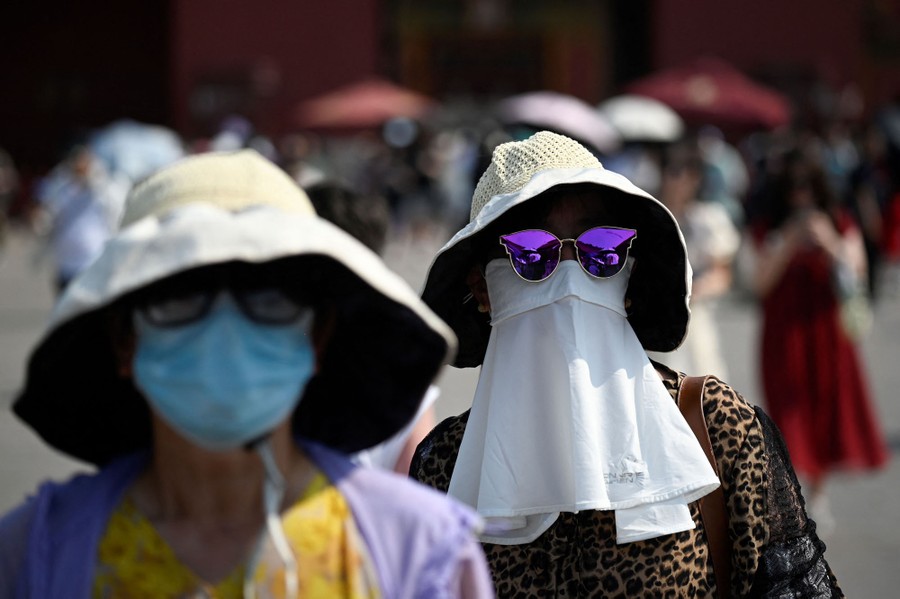 Two people wear big hats and masks on a hot day.