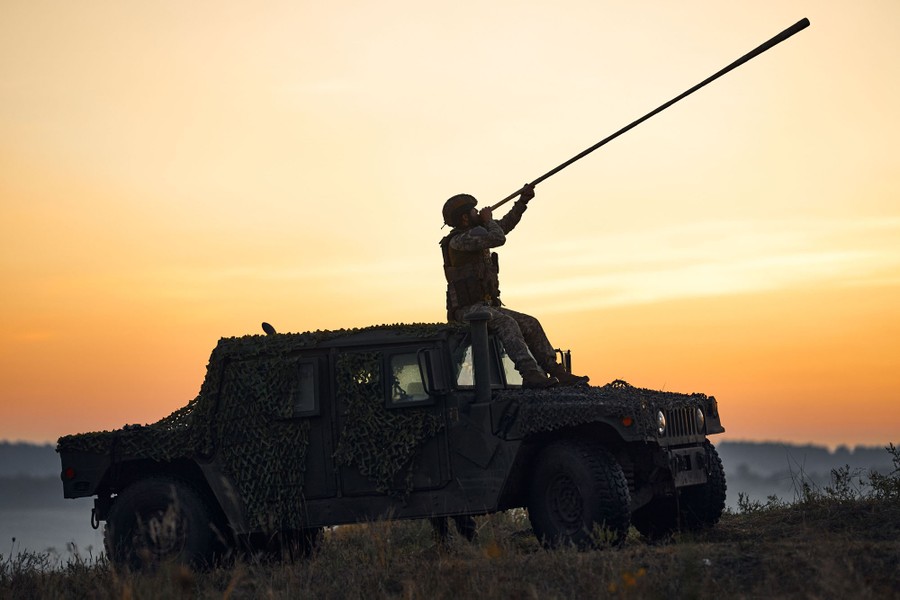 A soldier sits atop a military vehicle while playing a very long wooden horn.