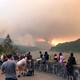 People watch a wildfire burning in a mountain range.