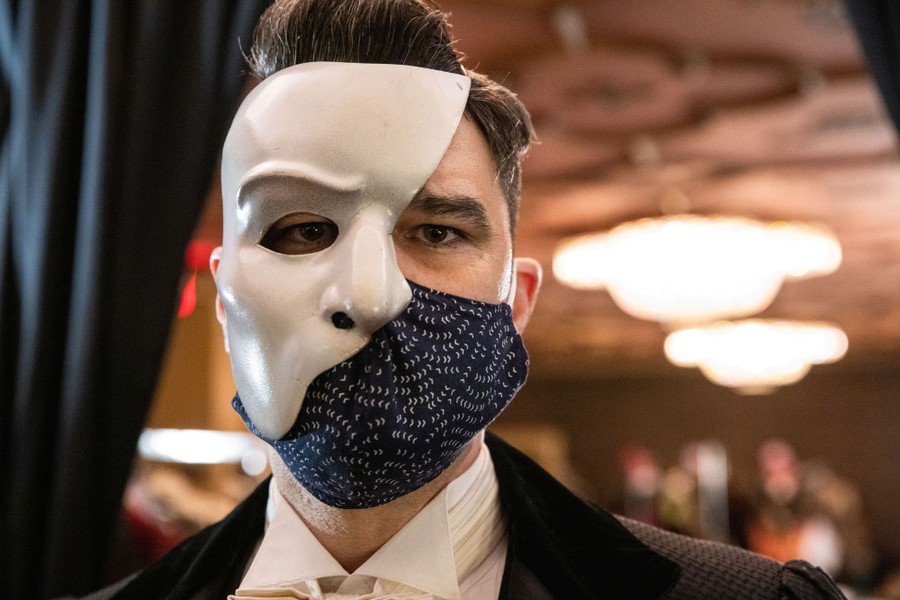An actor poses while wearing both a protective mask and a prop mask.