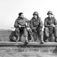 Three U.S. soldiers sit together on a wall during World War II.