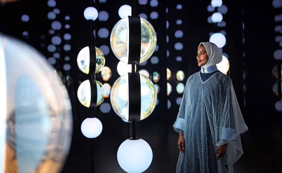A person stands inside a dark room, looking at suspended globes, lit up in an exhibition.
