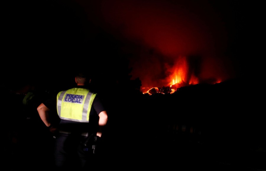 A police officer watches a volcanic eruption at night.