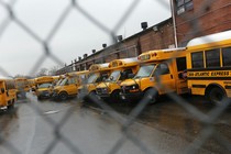 School buses photographed through a chain-link fence.