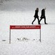 Two people walk together in a snowy NYC park behind a sign that says: "Keep this far apart."