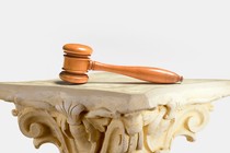 A gavel atop a Greek-looking column