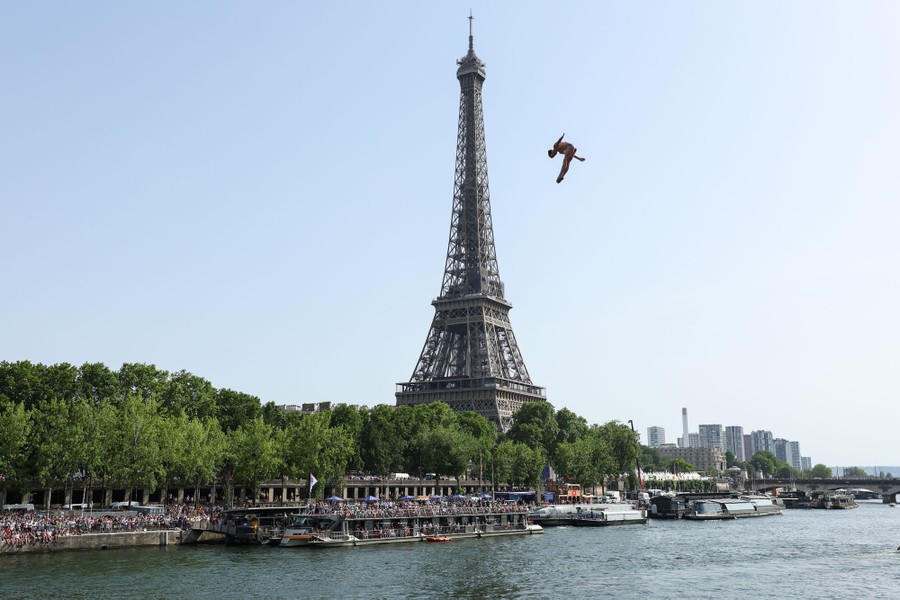 A diver falls from a height above a river near the Eiffel Tower.