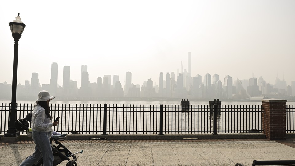 A woman pushes a stroller, with smoky air in the background