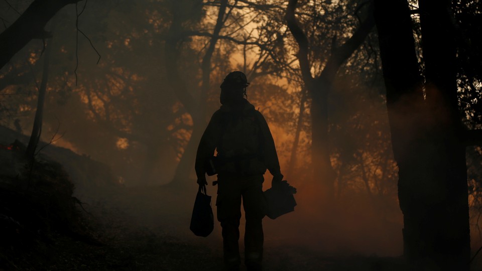 A firefighter walks through a dark, smoky forest