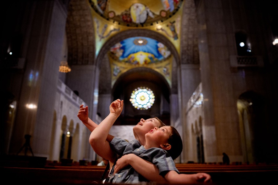 A woman holds a child in her arms as they both look up toward the ornate ceiling of a basilica.