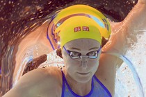 A close view of a swimmer's face, seen from below, underwater, as they swim in a race