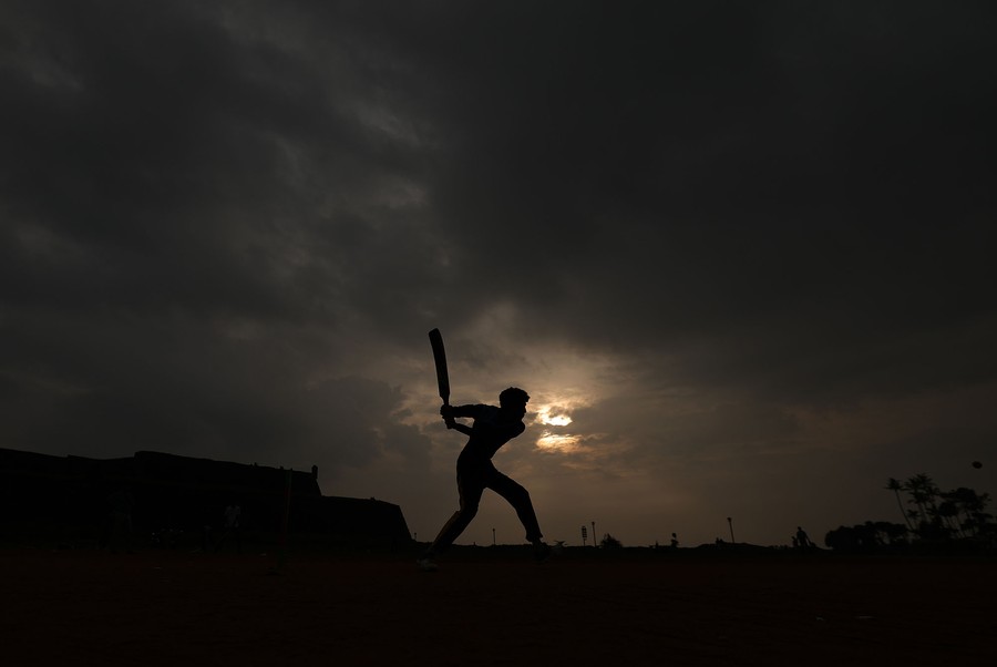A cricket player in silhouette holds up a bat.
