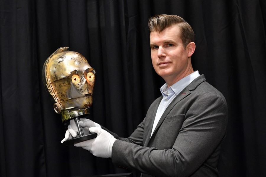 A person holds up a movie prop, the head of the robot C-3PO from the Star Wars franchise.