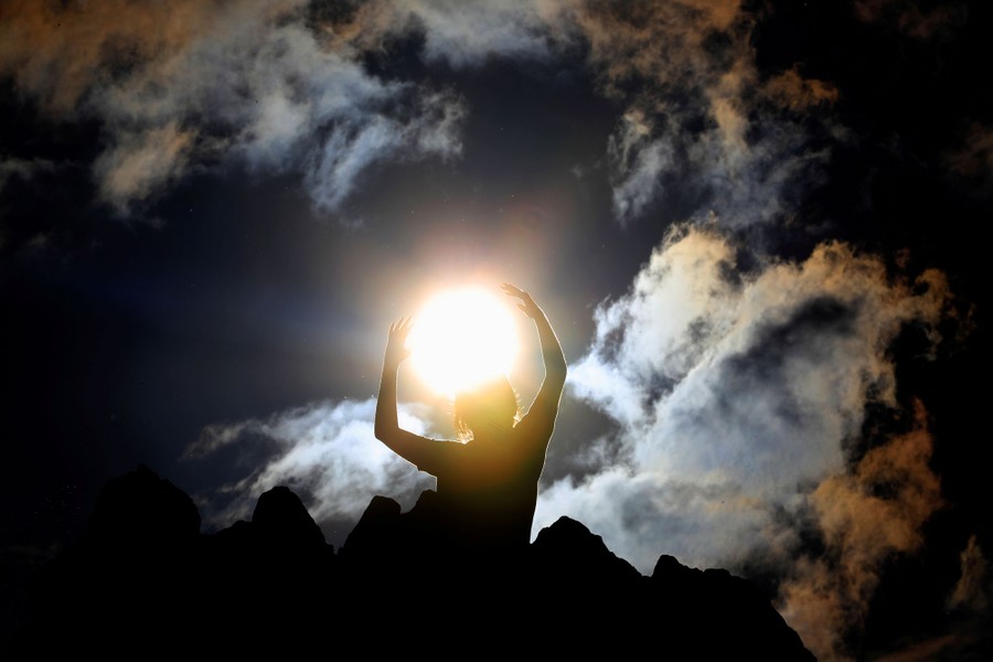 A person poses with their arms in the air, appearing to hold the sun.