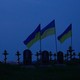 Photo of a cemetery with crosses and Ukrainian flags visible against a dark sky
