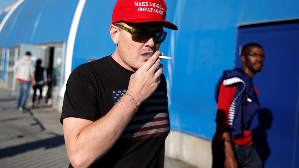 A man in a "Make America Great Again" cap smokes a cigarette. 