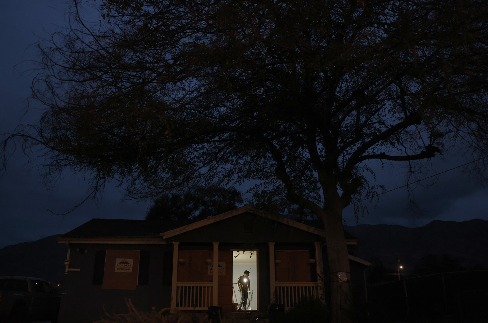 A person is seen working inside a house, viewed from outside, through an open door, at night.